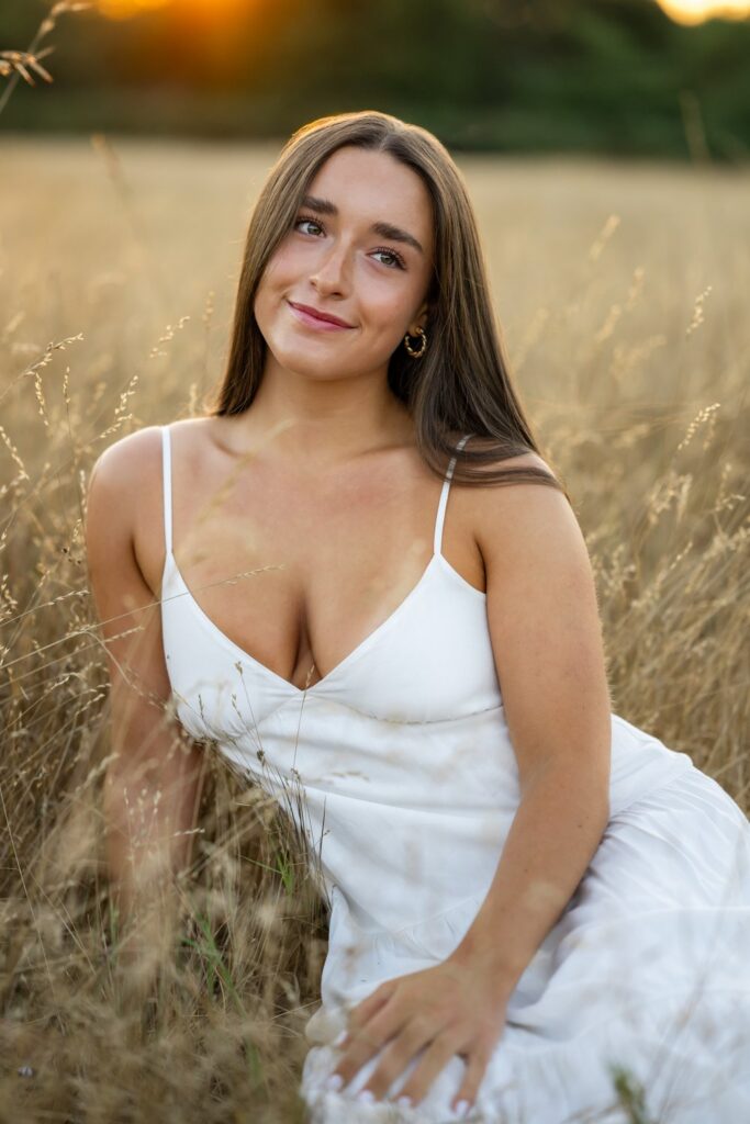 senior girl in white dress sitting in open field at discovery park seattle