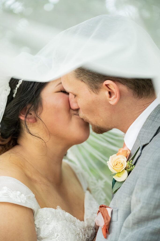 bride and groom under veil kiss