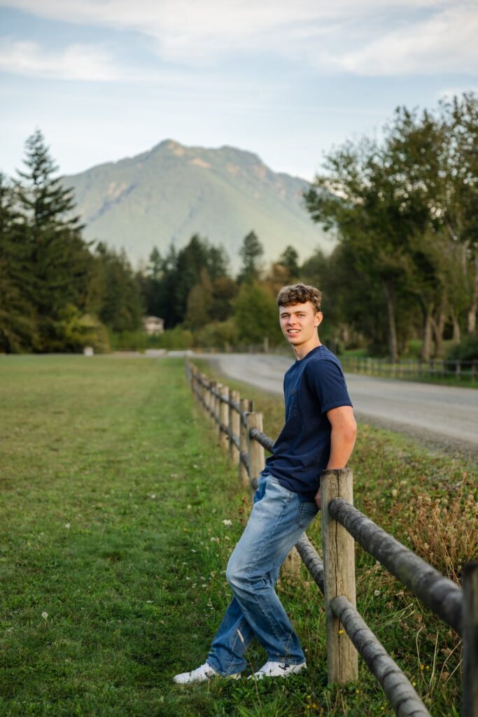 senior guy leaning on fence with mount si in background